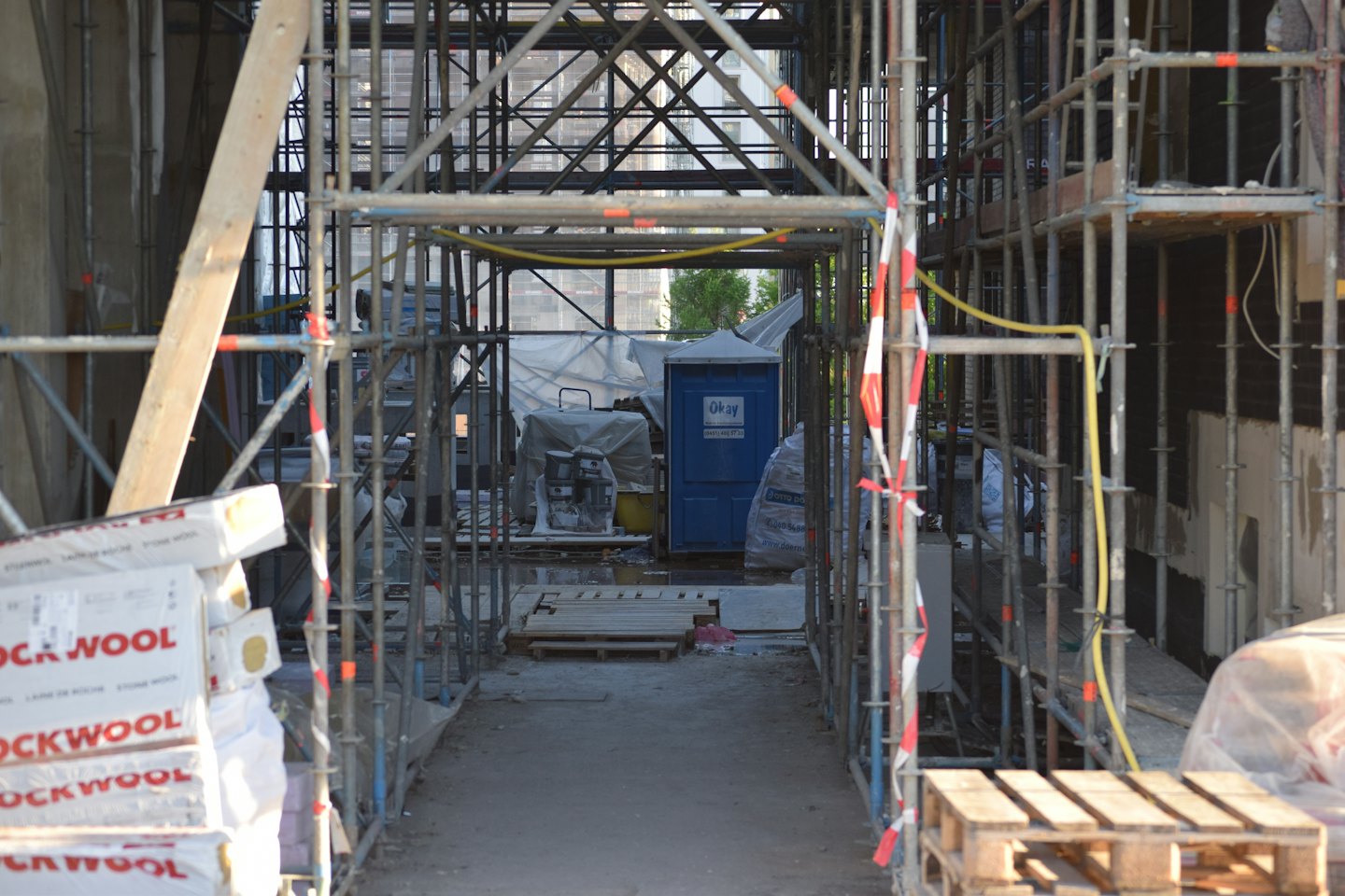 Construction materials and a porta-potty sit inside a scaffolding tunnel.